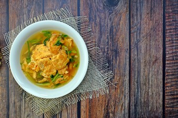 Clear soup with Thai omelette in white bowl on wooden table. Authentic Thai food.