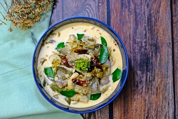 Snakeskin gourami and young tamarind leaf in coconut milk in dark blue bowl n wooden table. Authentic Thai food.