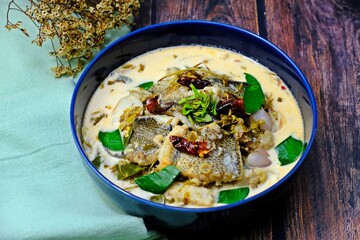 Snakeskin gourami and young tamarind leaf in coconut milk in dark blue bowl n wooden table. Authentic Thai food.