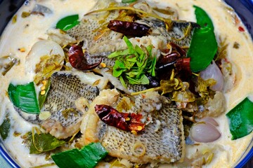 Snakeskin gourami and young tamarind leaf in coconut milk in dark blue bowl n wooden table. Authentic Thai food.
