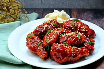 Crispy and crunchy Korean fried chicken wings (Dakgangjeong) in white plate on wooden table.