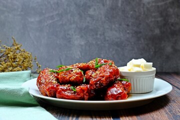 Crispy and crunchy Korean fried chicken wings (Dakgangjeong) in white plate on wooden table.