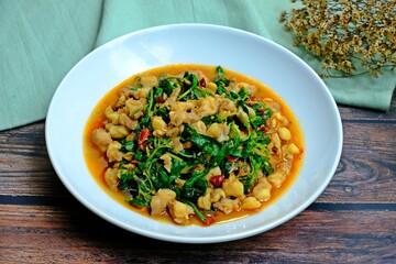 Stir fried chicken tendons with holy basil in white plate on wooden table. Authentic Thai food.