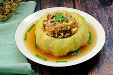Stuffed cabbage soup with minced pork mixed with flavoring in white bowl on wooden table.