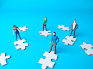 Miniature people and white jigsaw puzzle on a blue background.