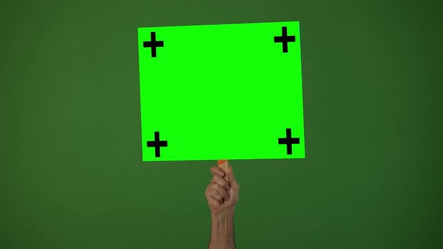 Arm holding a green screen sign with tracking points on a chroma key background.