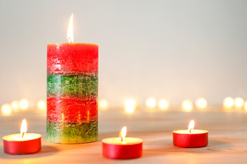 Christmas red and green candle and tealights on wooden table at home with defocused holiday lights in background, copy space for text