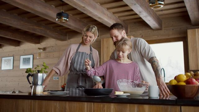 Small girl with parents cooking together indoors, winter holiday in private apartment.