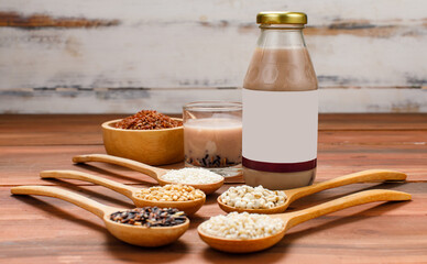 Fresh organic fruit extract drink in glass bottle beside wooden spoon of natural cereal grains, bean ingredient, and bowl of brown rice