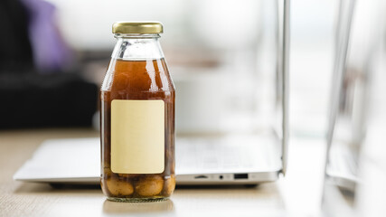 Fresh nourishment drink extract from natural organic ginkgo and longan in glass bottle product with blank logo served on laptop working desk for refreshment beverage of invigoration