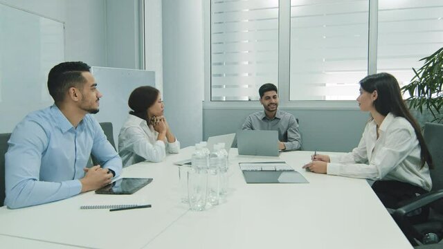 Indian businessman talking to business people colleagues or partners sitting at conference table, male leader discussing work at team meeting or group negotiations having conversation with clients