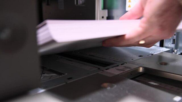 Male businessman worker loading a pack of white paper for printing into an industrial printer