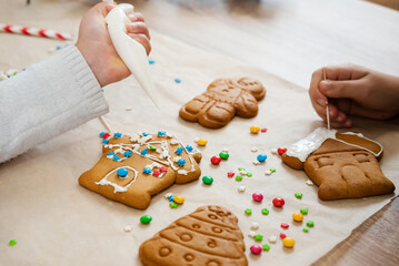 Child is decorating honey gingerbread cookies on table at kitchen. Icing of Christmas bakery.