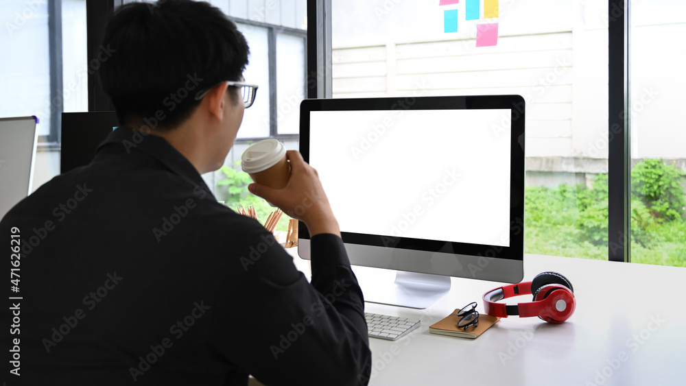 Poster rear view of businessman drinking coffee and working with computer.