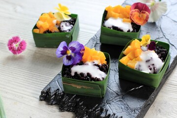 Homemade Coconut Black Sticky Rice with Mango in Pandan Leaves Cup, Selective Focus with Pansies Edibel Flower Topping