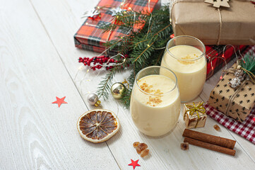 Two glasses of eggnog on a white wooden table next to the Christmas presents. Sweet egg dessert. Christmas breakfast.