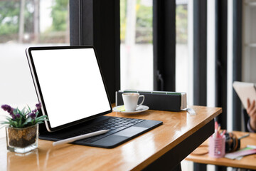 Computer tablet with white screen, coffee cup and book on wooden table.