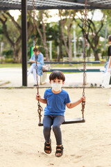 A cute Asian boy wearing a mask is playing on a swing in the playground during the daytime in summer. Outdoor activities. Play Makes Ideas Believe External education. portrait
