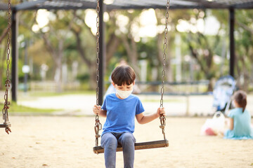 A cute Asian boy wearing a mask is playing on a swing in the playground during the daytime in summer. Outdoor activities. Play Makes Ideas Believe External education. portrait