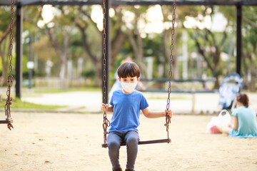 A cute Asian boy wearing a mask is playing on a swing in the playground during the daytime in summer. Outdoor activities. Play Makes Ideas Believe External education. portrait