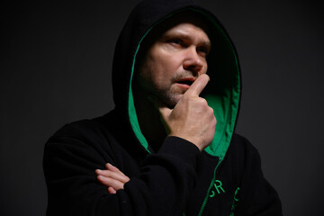 Portrait of a serious pensive man in a hood in the dark looks to the side