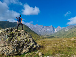 A man watching the sharp mountain peaks of the Chaukhi massif in the Greater Caucasus Mountain Range in Georgia, Kazbegi Region. The hiker stands on a massive rock. Georgian Dolomites. Freedom