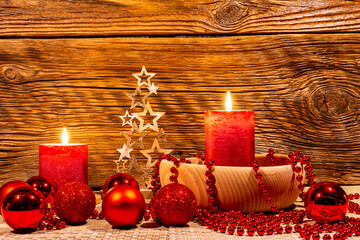 Christmas decoration. Lantern, golden Christmas tree and red bubbles, lit candles, cones on the background of a wall of old damaged wood.