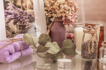 Spa still life with herbs and essential oil in glass jars, towel, perfumed candle and eucalyptus leaves on glass surface.