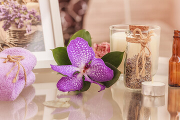 Lavender spa lilac composition. orchid flower , towel, bottle of lavender herbs, white candle in glass, floral picture in the white frame on glass table. 