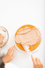 Culinary confectionery. Top view female hands of cook decorating cake with cream filling using spatula, housewife preparing layered delicious cake in kitchen indoors, copy space for text