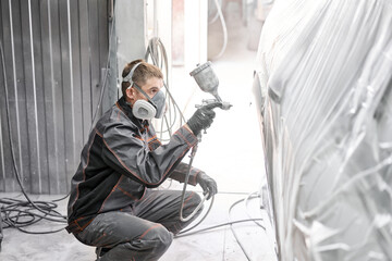 Painting the rear part of the car. Car painter wearing costume and protective gear. Car service station. Restoring a car after an accident