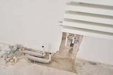 connection heating pipes to white Radiator in a new apartment under construction. Work As A Plumber, mounting water heating radiator on the white wall indoors