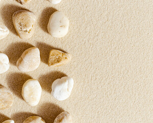 Fototapeta na wymiar Sea stones neutral beige color on natural fine sand background with copy space. Natural white yellow pebbles, monochrome tones. Spa minimal background