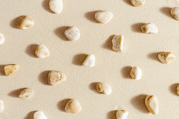 Pattern with pebble sea stones on fine sand. Natural stone neutral beige yellow color, monochrome tones. Summer minimal design background