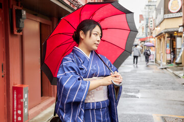 傘を持って東京の下町を歩く着物姿の日本人女性