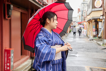 傘を持って東京の下町を歩く着物姿の日本人女性