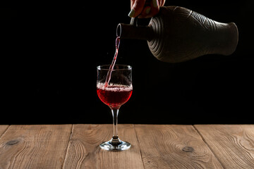 girl hands pouring red wine into a glass from a clay bottle on a black background