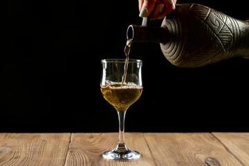 girl hands pouring red wine into a glass from a clay bottle on a black background
