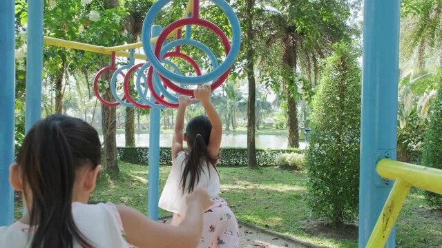 Happy little girls having fun on colorful bar at outdoor playground. Active kid hang on colorful monkey bars in the park. Play is learning in childhood.