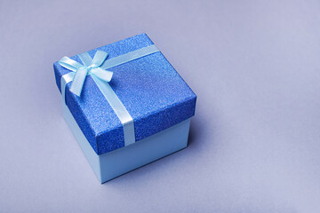 Blue gift box with a bow on a gray background. Holiday greeting card.