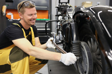 Smiling locksmith with wrench near motorcycle wheel in car workshop