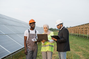 Muslim woman in hijab and indian man in white helmet talking with african american technician on...