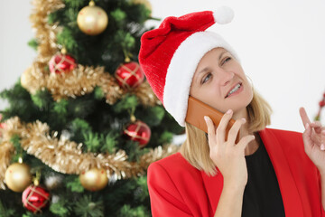 Businessman is talking on phone in santa claus hat against background of New Year tree