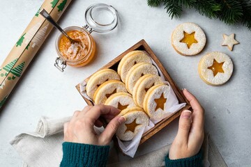 Linzer Christmas or New Year cookies filled with orange jam and dusted with sugar in box on grey background. Traditional Austrian Christmas cookies. Shortbread cookies. Homemade sweet present in hand.