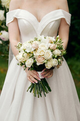 The bride in a wedding dress with open shoulders holds a bouquet of roses