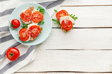 Italian food concept. Open sandwiches with mozzarella, tomatoes and arugula on white wooden background. Flat lay, copy space