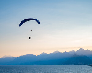 Silhouette of a man on a paraglider flying over the sea at sunset.