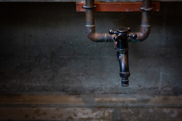 Old black faucet with rust marks in a dark atmosphere.