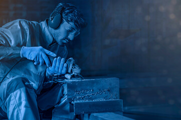 Young man doing work with electric wheel grinding on steel structure in factory