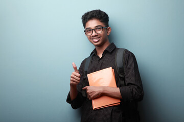 Smiling boy of Indian ethnicity holding note books in his hands and shows thumbs up gesture © AJay